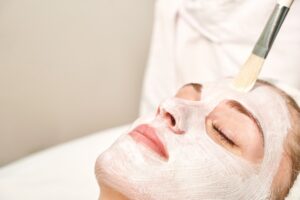 Close-up of a woman receiving a facial with white product covering her face and a brush applying the product